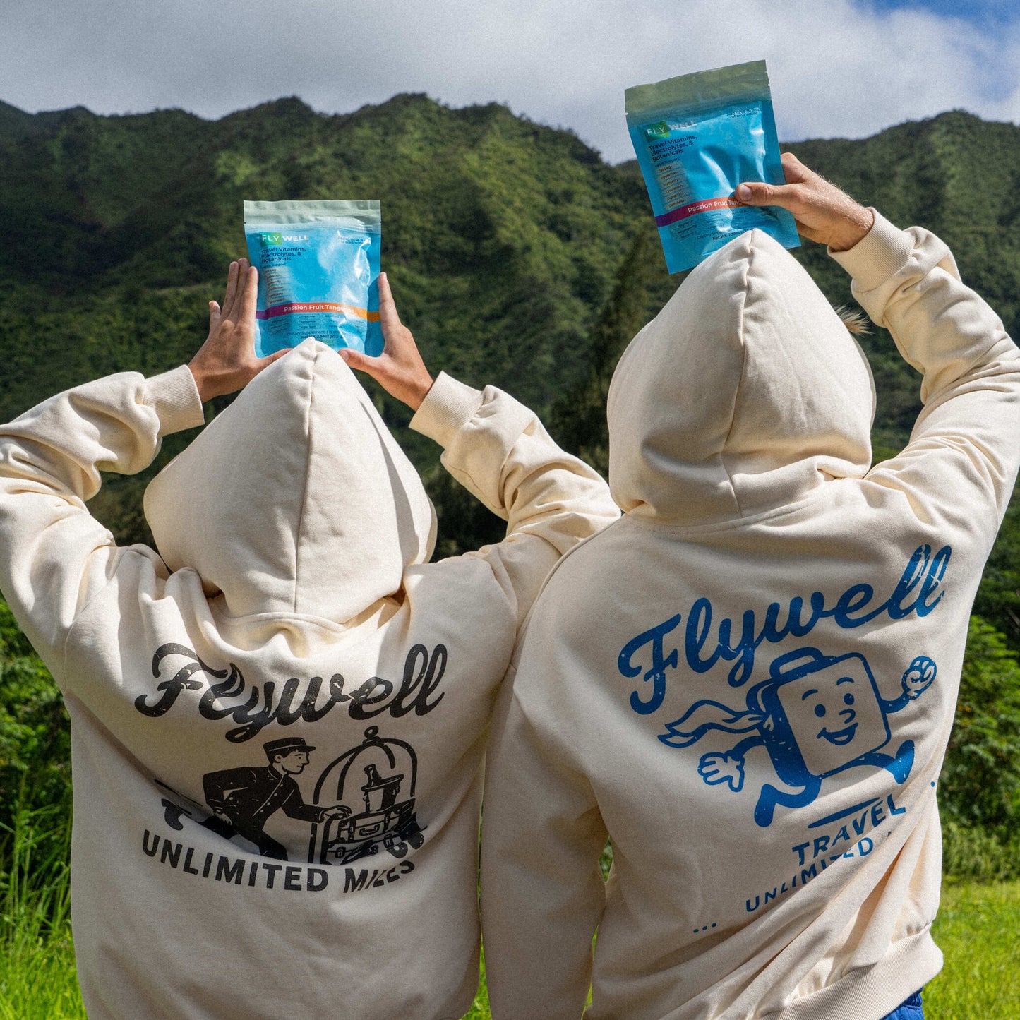 Two people wearing 'Flywell' branded hoodies with mountainous landscape in the background