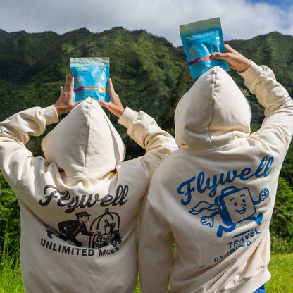 Two people wearing 'Flywell' branded hoodies with mountainous landscape in the background