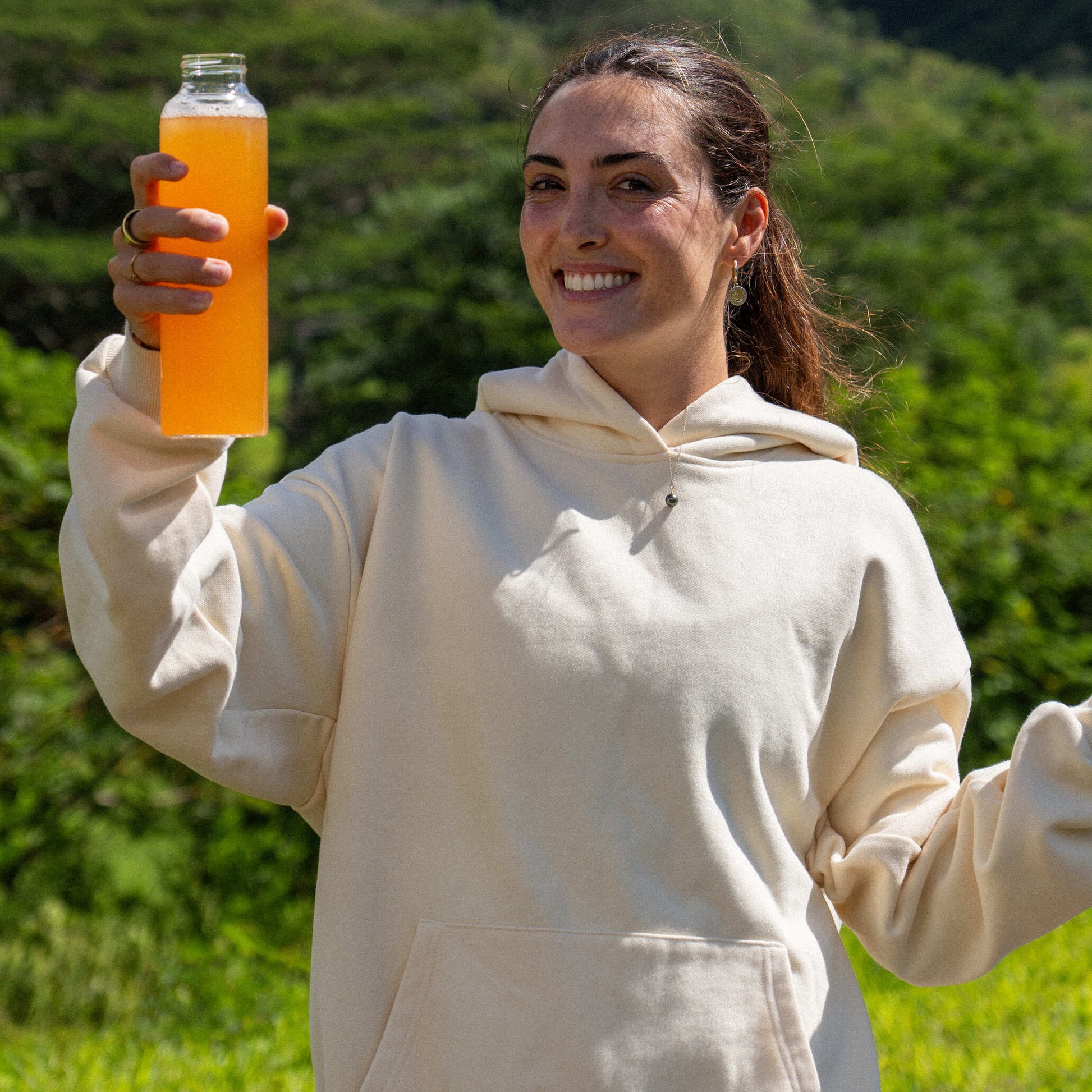 Woman holding an orange juice bottle outdoors with greenery in the background