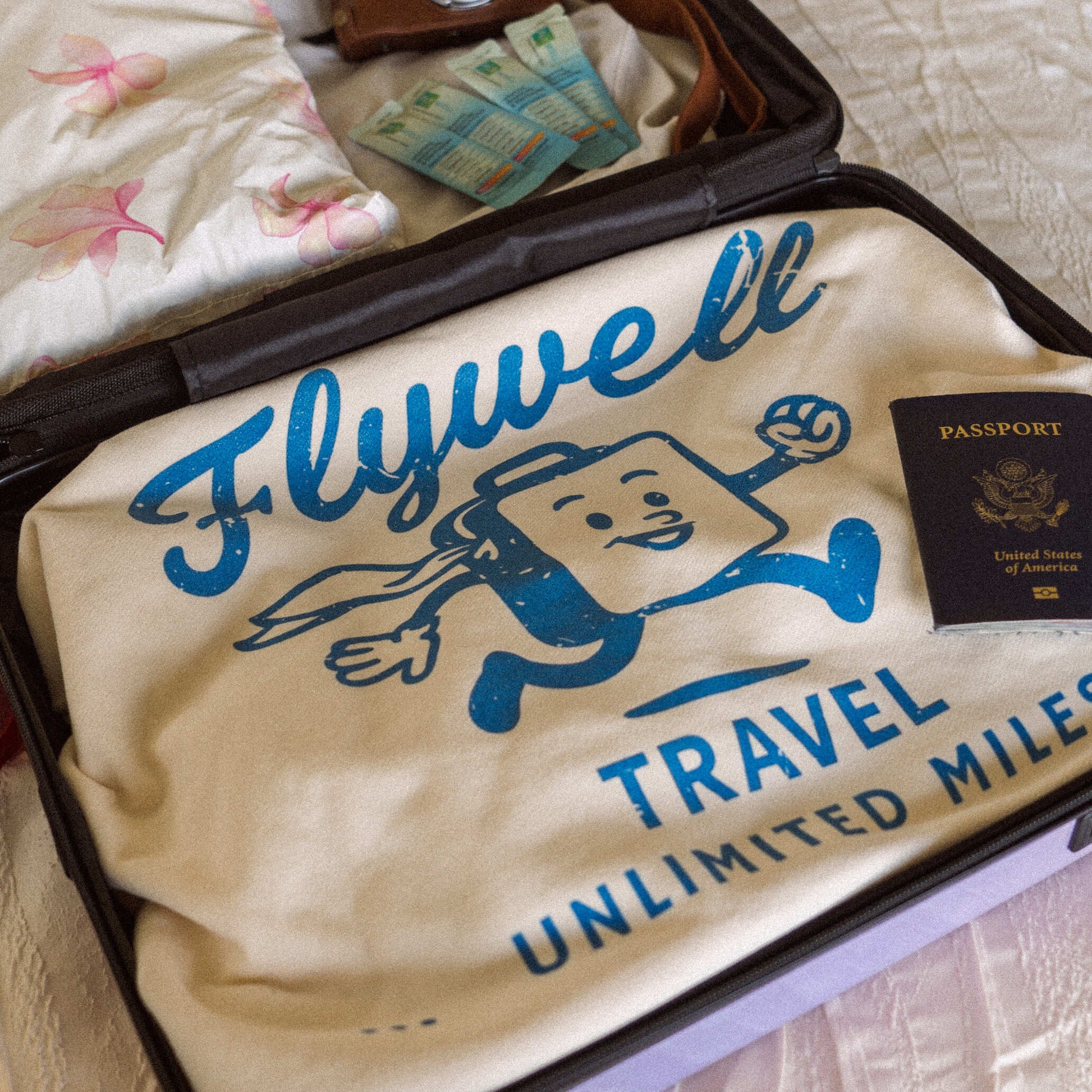 Open suitcase with 'Flywell Travel Unlimited Miles' bag and passport on a bed.