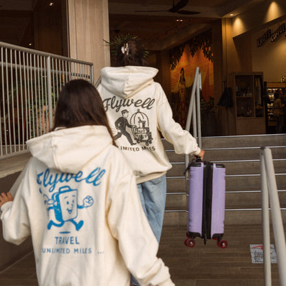 Two people wearing 'Flywell' branded hoodies with purple suitcases in a hotel.