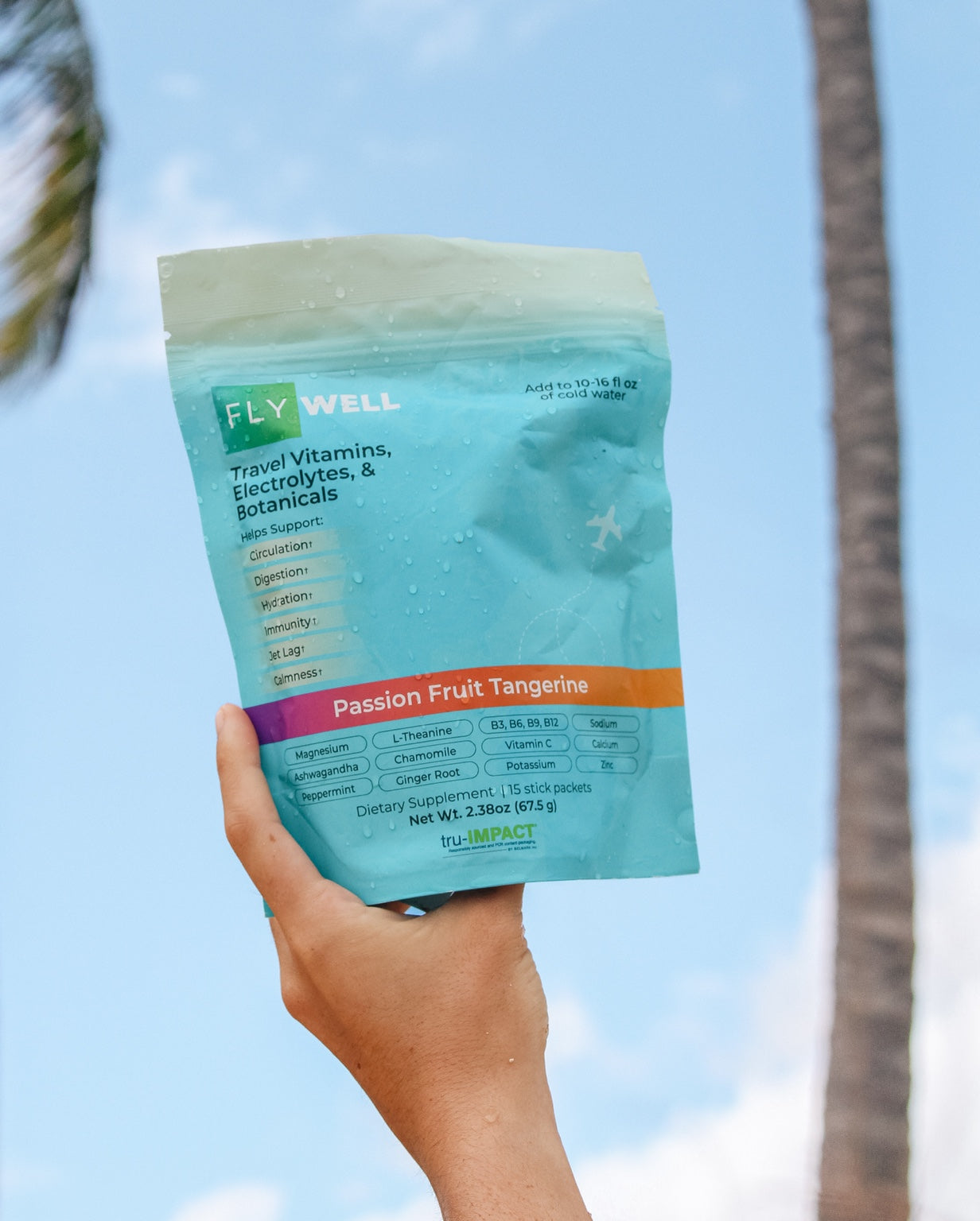 FlyWell Passion Fruit Tangerine pouch held against blue sky and palm trees