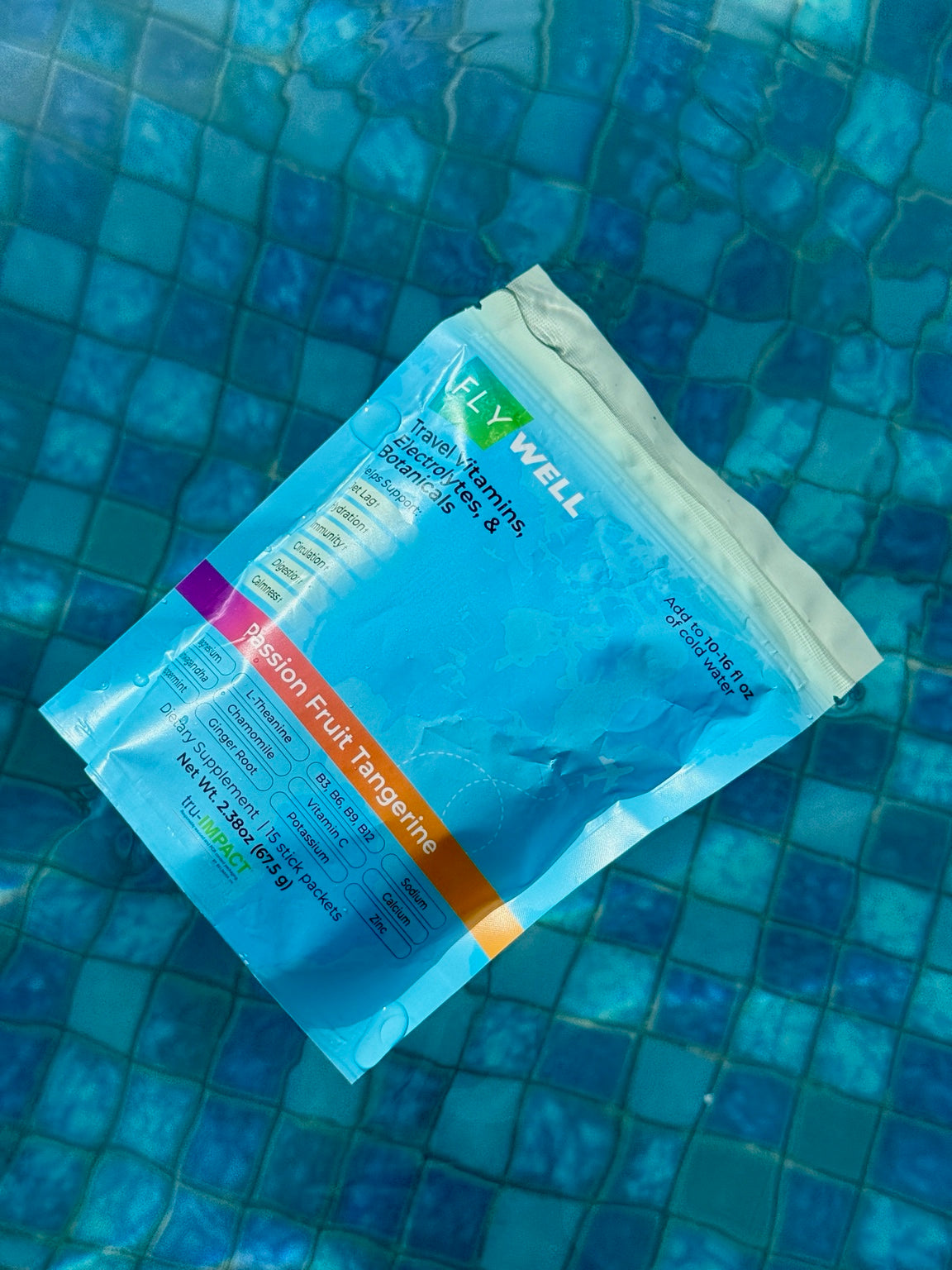 FlyWell Passion Fruit Tangerine pouch floating in a pool over blue tiles